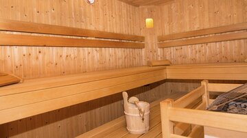 Eine gemütliche Sauna mit Holzverkleidungen und Bankbänken. In der Mitte steht ein Eimer und ein Saunaofen.
