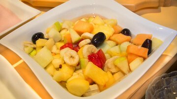 Eine Schüssel mit frischem Obstsalat, die verschiedene geschnittene Früchte wie Melone, Banane und Trauben enthält. Der Salat ist bunt und appetitlich präsentiert.