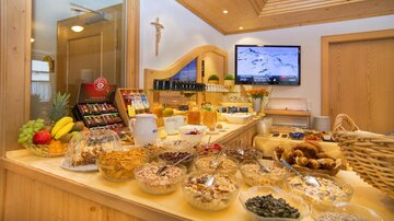 Ein einladendes Frühstücksbuffet mit einer Auswahl an Obst, Müslis und Gebäck. Im Hintergrund ist ein Fernseher zu sehen, der eine schöne Atmosphäre schafft.