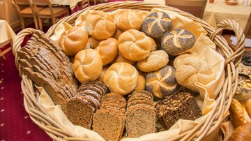 Ein Korb mit verschiedenen Brotsorten, darunter Brötchen und Vollkornbrot. Die Brote sind frisch und appetitlich angerichtet.