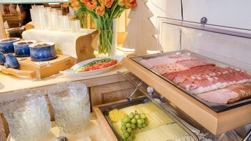 Ein liebevoll angerichtetes Buffet mit verschiedenen Aufschnittsorten, frischem Obst und Gemüse. Im Hintergrund stehen bunte Tulpen in einer Vase.