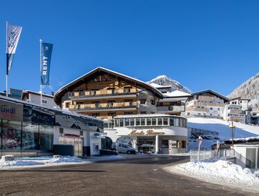 A picturesque mountain village in winter with snow-covered houses and a clear blue sky. In the foreground, the "Alpenresort" hotel can be seen.