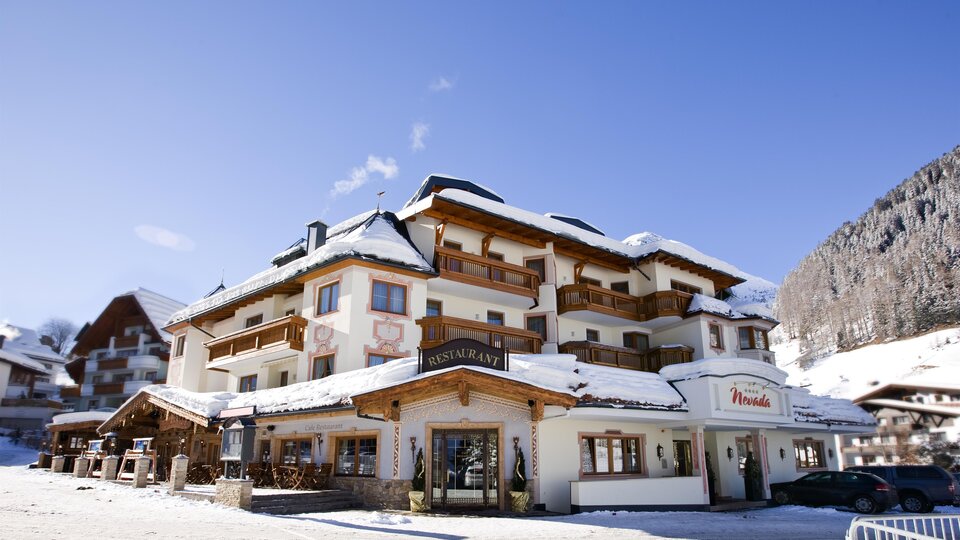A cozy hotel in a snowy landscape. The facade is designed in a traditional style with balconies and wooden details.