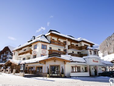Ein gemütliches Hotel in einer verschneiten Landschaft. Die Fassade ist im traditionellen Stil mit Balkonen und Holzdetails gestaltet.