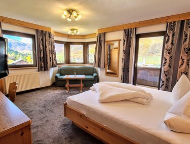 A cozy hotel room with a double bed and a living area. Large windows offer views of the surrounding landscape.