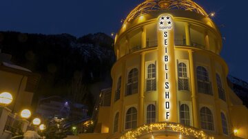 Ein schönes, beleuchtetes Gebäude mit der Aufschrift „SEIBLISHOF“. Es befindet sich in einer bergigen Umgebung und ist abends fotografiert.