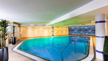 Ein eleganter Innenpool mit grün-blauem Wasser und modernem Design. Pflanzen und sanfte Beleuchtung sorgen für eine entspannte Atmosphäre.