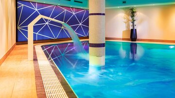 Ein moderner Innenpool mit klarem Wasser und ansprechendem Design. Im Hintergrund sind geometrische Muster und Pflanzen zu sehen.