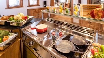 Eine moderne Küche mit holzverkleideten Wänden und großen Fenstern. Auf der Arbeitsfläche stehen frisches Gemüse und Zubereitungsmaterialien.