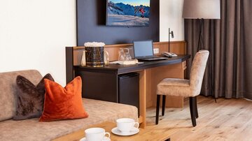 Ein modernes Zimmer mit einem Arbeitstisch und einem Fernseher an der Wand. Die Einrichtung ist stilvoll und gemütlich, mit einem Sofa und einer Stehlampe.