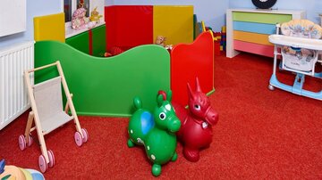Ein bunter Spielbereich für Kinder mit einer grünen und roten Spielzaun. Zwei Plüschspielzeuge in Form von Tieren stehen auf einem roten Teppich.