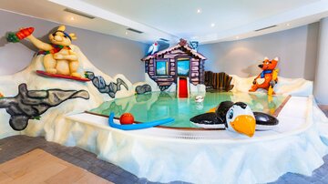 Ein farbenfrohes Indoor-Wasserbecken mit kindgerechten Spielzeugen. Es gibt eine Spielhütte und verschiedene aufblasbare Figuren in einer lustigen Umgebung.