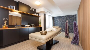 Ein modernes Wellnesszimmer mit einer Massageliege und stilvollen Akzenten. Der Raum ist hell und bietet eine entspannende Atmosphäre mit dekorativen Elementen.