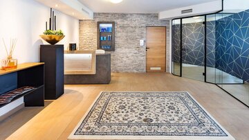 Eine moderne Empfangshalle mit Steinwand und stilvollem Empfangstresen. Der Boden ist mit einem dekorativen Teppich und warmen Holztönen gestaltet.