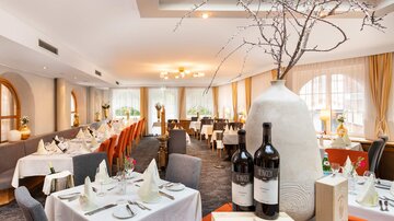 Ein elegantes Restaurant mit weißen Tischdecken und stilvollen Stühlen. Auf den Tischen stehen Weinflaschen und dekorative Elemente.