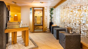 Ein moderner Wellnessbereich mit einer Sauna und einem minimalistischen Design. Die Wände sind mit dekorativen Steinen und Pflanzen verziert.