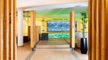 Ein moderner Wellnessbereich mit Holzsäulen und einer sanften Beleuchtung. Im Hintergrund ist ein beleuchteter Pool zu sehen.