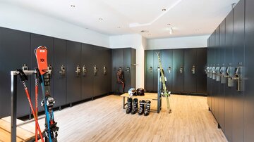 Ein moderner Umkleideraum mit schwarzen Schränken und Holzfußboden. Ski-Equipment ist ordentlich aufgestellt und bereit zur Nutzung.