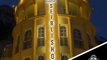 Ein elegantes Hotelgebäude mit beleuchteter Fassade und einem goldenen Kuppeldach. Das Schild "Seibilshof" strahlt in der Nacht und zeigt die Sterne-Bewertung.