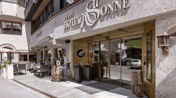 A modern hotel named "Hotel Sonne" in a picturesque setting.  
Tables and chairs stand invitingly in front of the entrance.