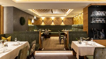 A stylish restaurant with elegant tables and cozy benches. Soft lighting creates an inviting atmosphere.