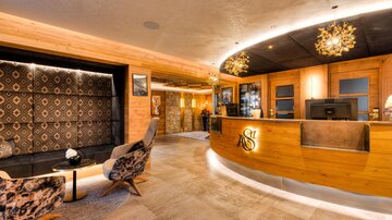 A modern hotel reception with wooden details and stylish furnishings. The lighting creates a warm, inviting atmosphere.