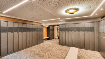 A modern designed changing room with several lockers and a beige floor covering. The walls are bright and elegantly lit.
