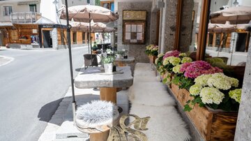 A cozy café with a wooden terrace, surrounded by colorful flowers. The tables are equipped with umbrellas and invite you to linger.