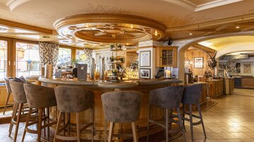 An elegant bar with a round counter and stylish seating. The space is bright and inviting, with decorative elements and windows that let in natural light.