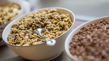 A bowl of muesli containing chocolate chips is in the foreground. In the background, there are more bowls with different types of cereal.