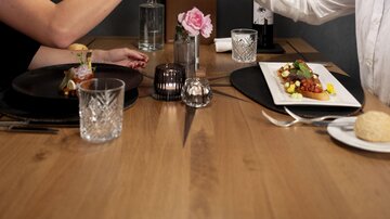 An elegant dinner couple raises their wine glasses in a stylish setting. The table is lovingly set with delicious food and decorative details.
