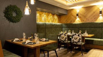 A modern restaurant with cozy green benches and stylish table decorations. The lighting creates an inviting atmosphere.