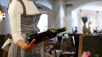 A waitress in traditional attire serves wine in an elegant restaurant. On the table are various delicious dishes and a glass of wine.