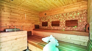 A modern sauna made of light wood with a cozy bench. Soft lighting and a relaxation area invite you to feel comfortable.
