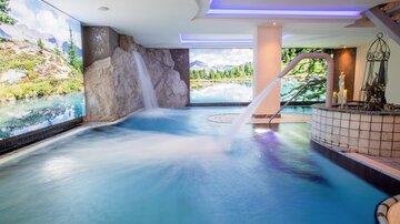 A modern wellness area with a pool and waterfall. The walls are decorated with landscape images that create a calming atmosphere.