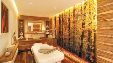 A modern spa with warm wooden tones and a calming forest wallpaper. The massage table is ready for relaxing treatments.