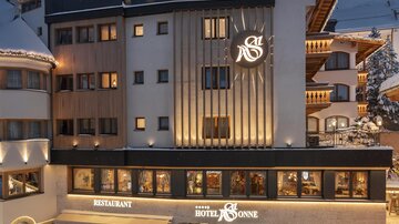 A modern hotel building in a winter atmosphere with snow-covered streets. The facade is illuminated and offers inviting dining areas.