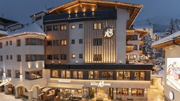 A modern hotel building in the snow, illuminated in the evening. On the ground floor, there is a restaurant with an inviting atmosphere.