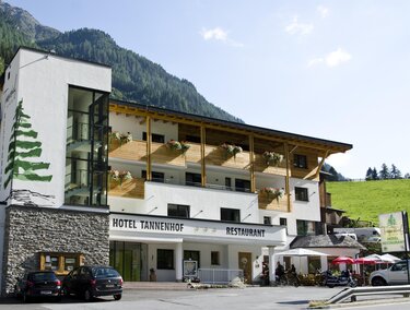 Ein modernes Hotelgebäude mit Holzverkleidung und einem großen Eingang. Das Hotel Tannenhof bietet auch ein Restaurant und liegt in einer malerischen Berglandschaft.